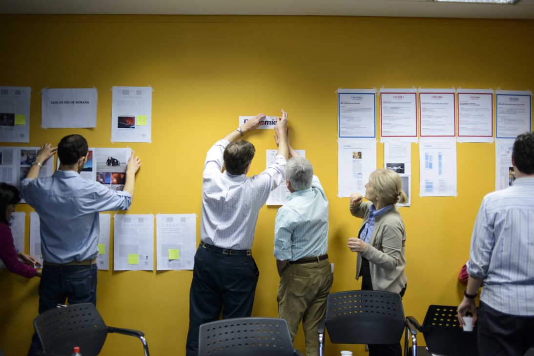 La Nación staff review redesign proposals pinned to a bright yellow wall during an innovation workshop.