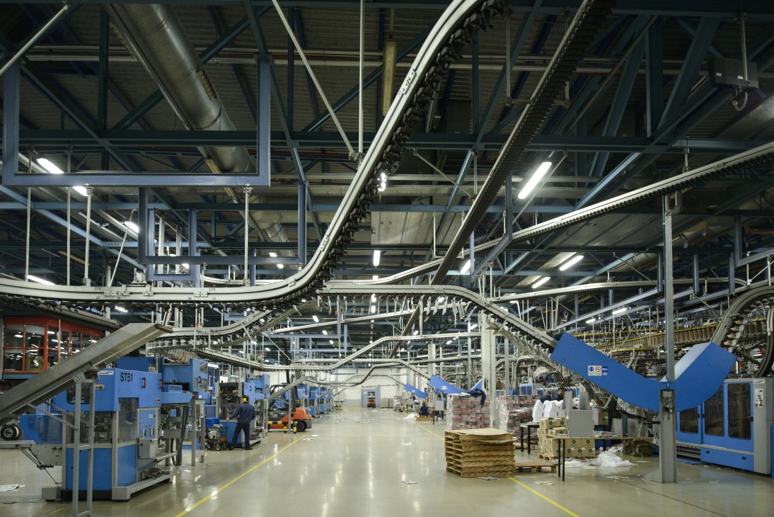 Industrial printing facility with blue machinery and overhead conveyor systems in a warehouse space.