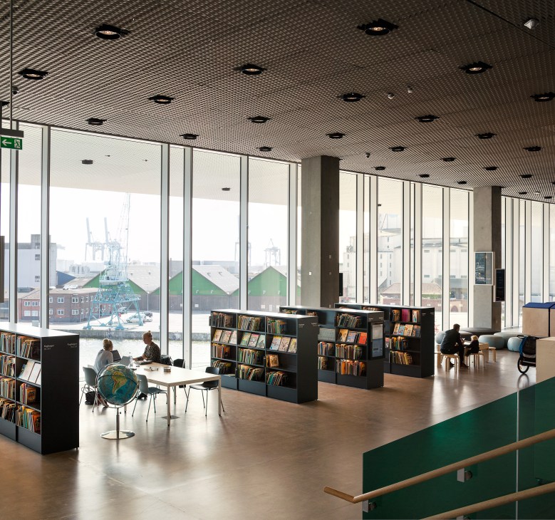 Interior of Dokk1 library with floor-to-ceiling windows overlooking Aarhus harbour and container cranes.