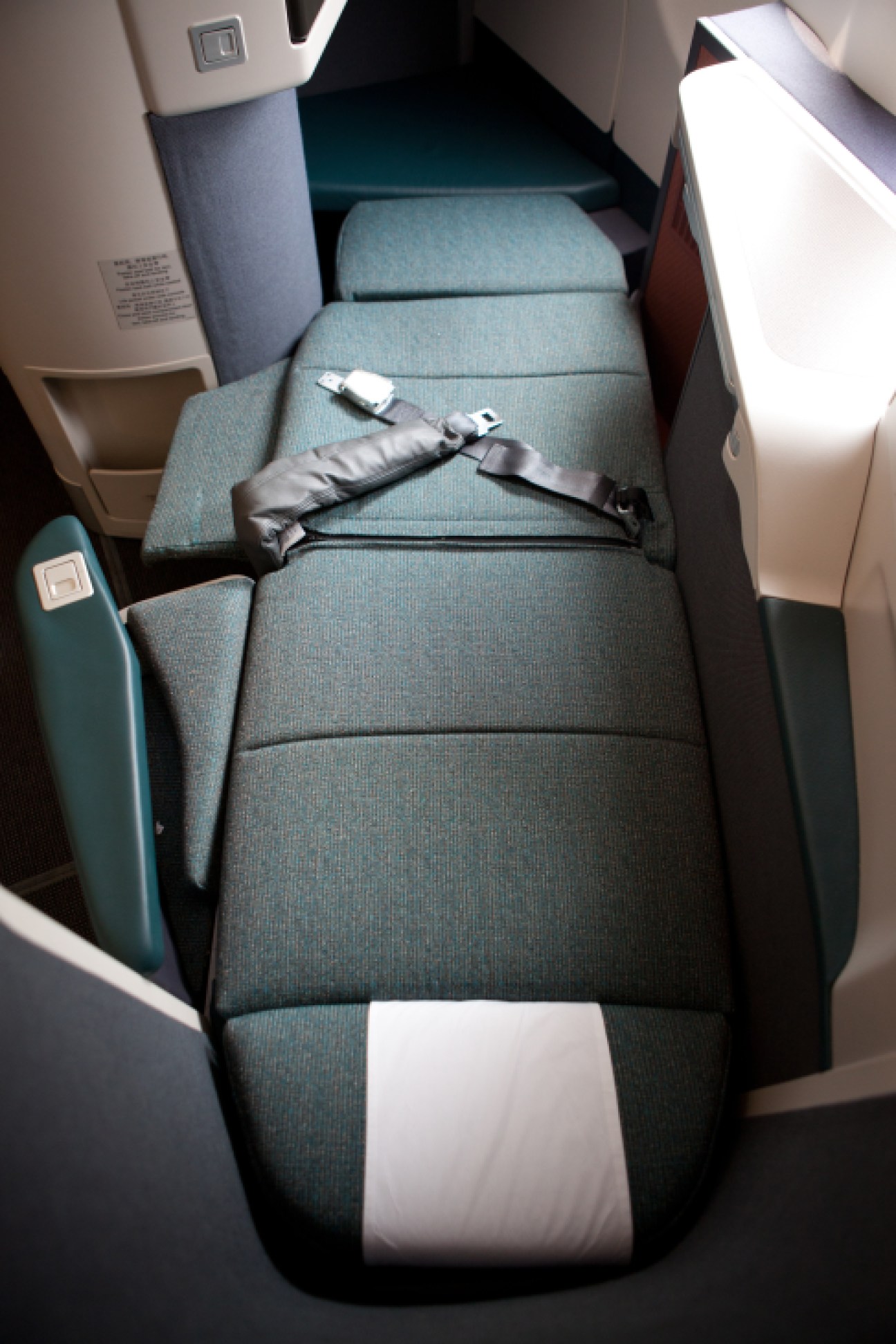 Overhead view of Cathay Pacific business class seat with teal upholstery, white pillow, and black amenity kit.