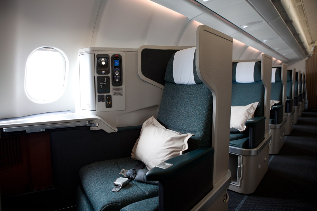 Cathay Pacific business class cabin with teal seats, white pillows, and modern beige dividers between individual pods.