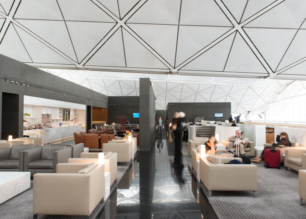 Modern airport lounge interior with geometric ceiling, cream seating areas, and natural light from skylight panels.