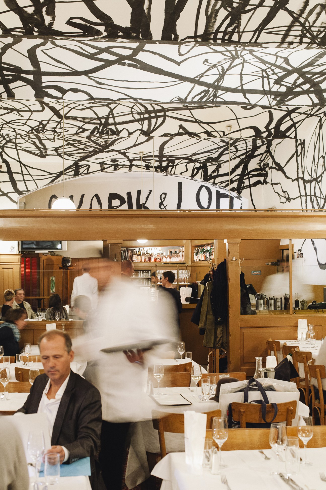Interior of Skopik & Lohn restaurant with dramatic black line artwork on ceiling and wooden furnishings.