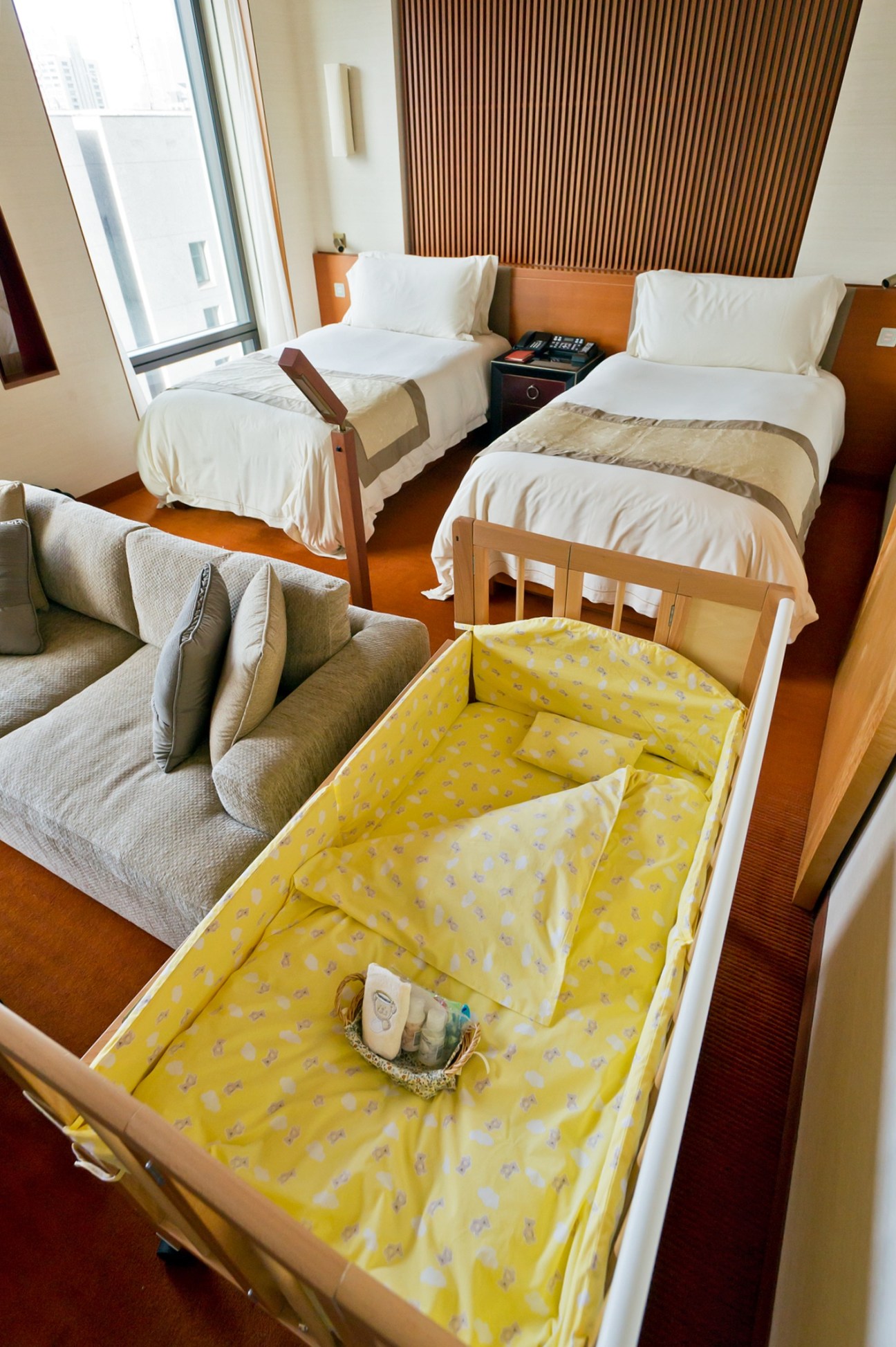Hotel room with wooden crib featuring yellow patterned bedding, two twin beds, and modern furnishings at Peninsula Tokyo.