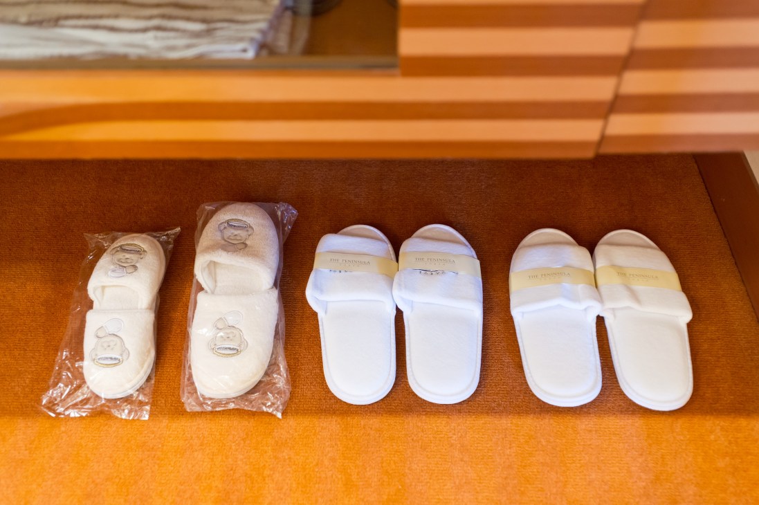 Six pairs of slippers in different sizes arranged on an orange fabric surface, showing Peninsula hotel amenities for guests.