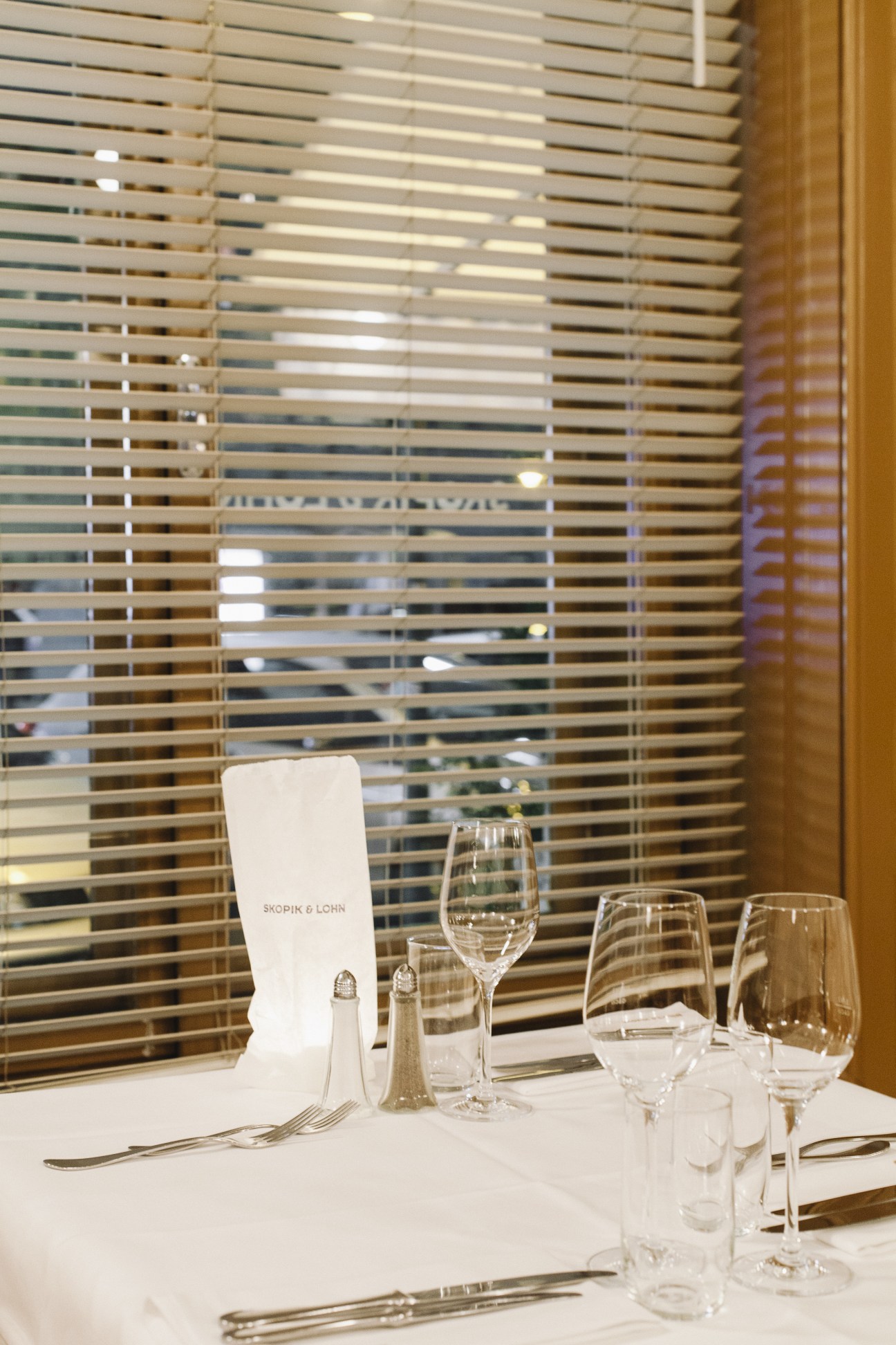Dining table setting at Skopik & Lohn restaurant with place card, wine glasses and slatted wooden screen backdrop.