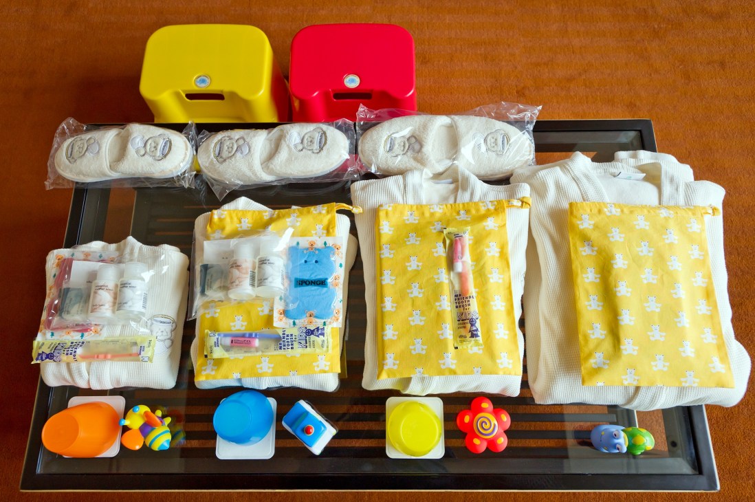 Overhead view of baby amenities displayed on a black tray including diapers, wipes, toys and toiletries.