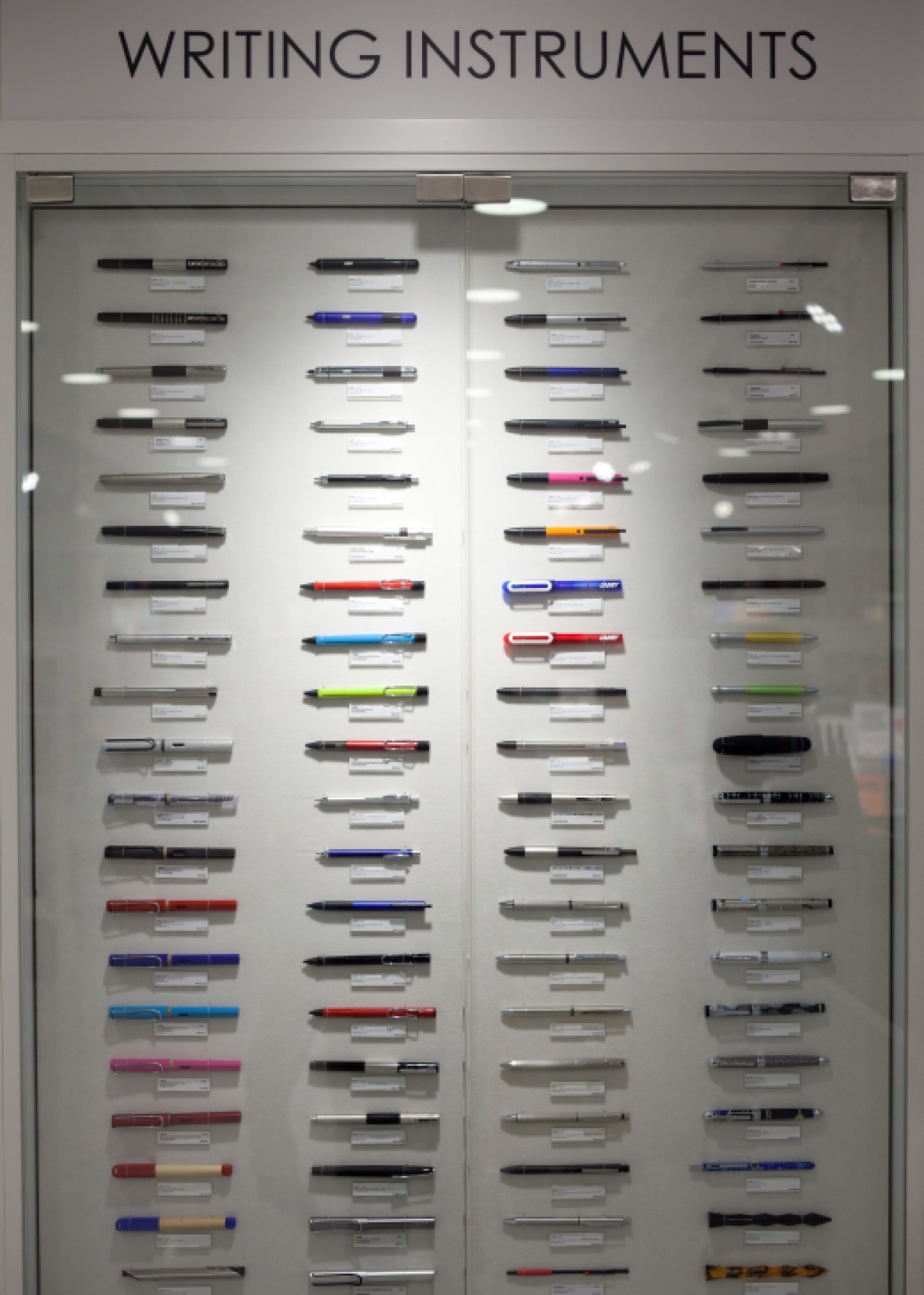 Museum display case of writing instruments organized in columns with product labels.