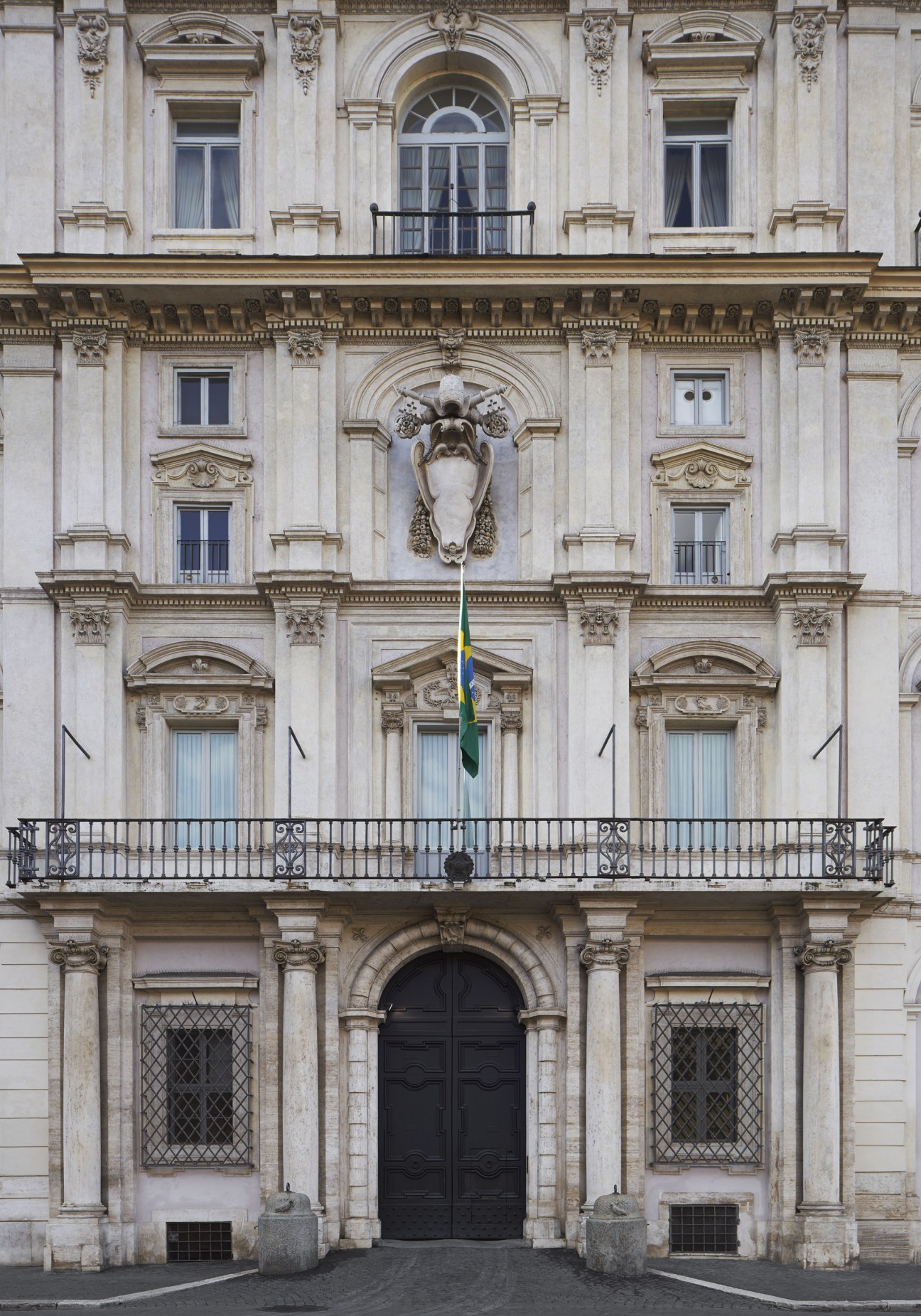 Neoclassical embassy facade with ornate stonework, arched windows, and a Brazilian flag hanging from a central balcony.