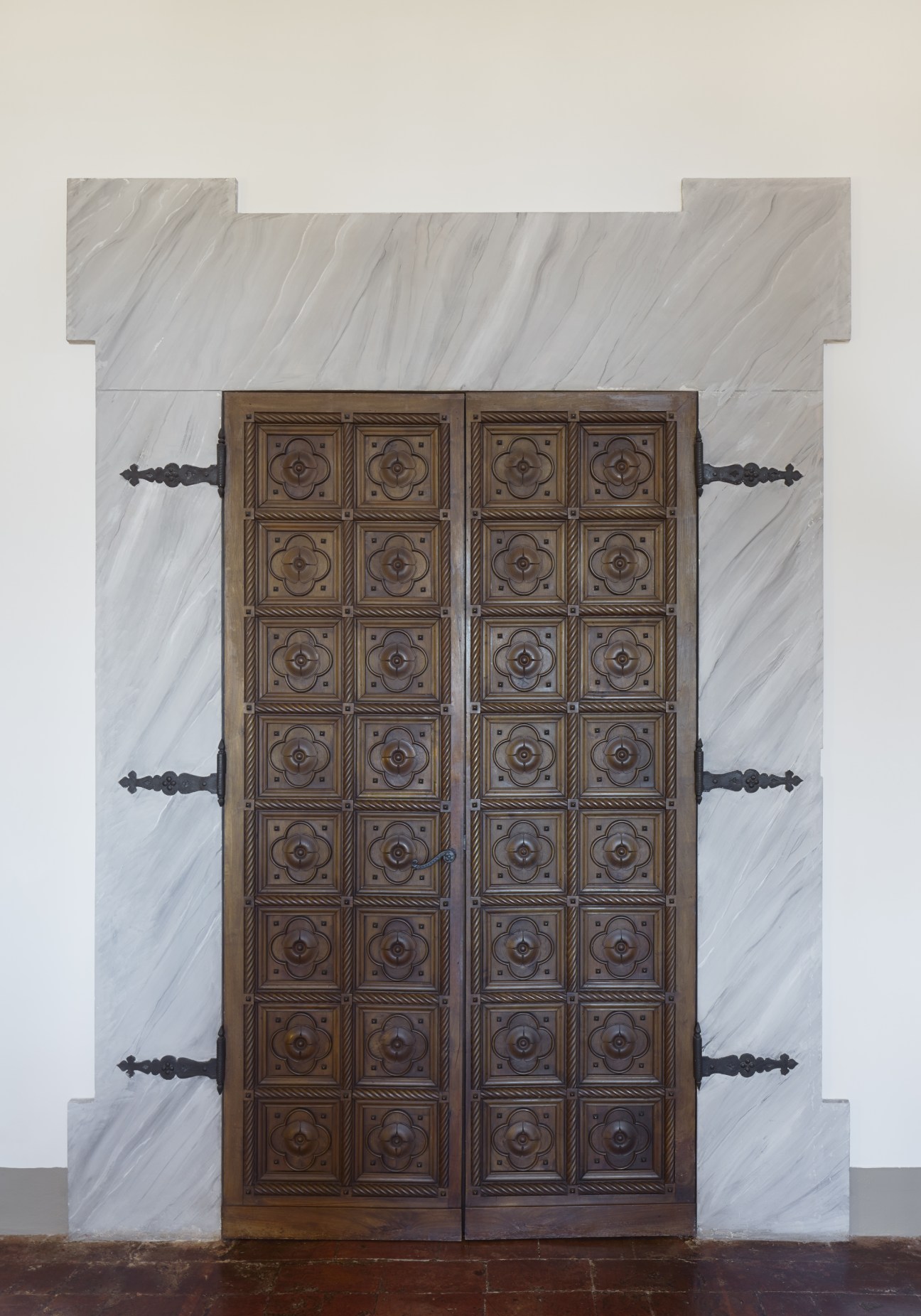 Ornate wooden double doors with carved geometric panels set in marble frame.