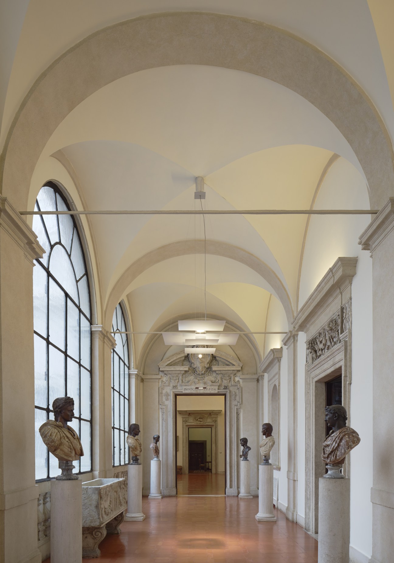 Grand hallway with vaulted ceiling, Roman emperor busts on pedestals, and arched architectural details.