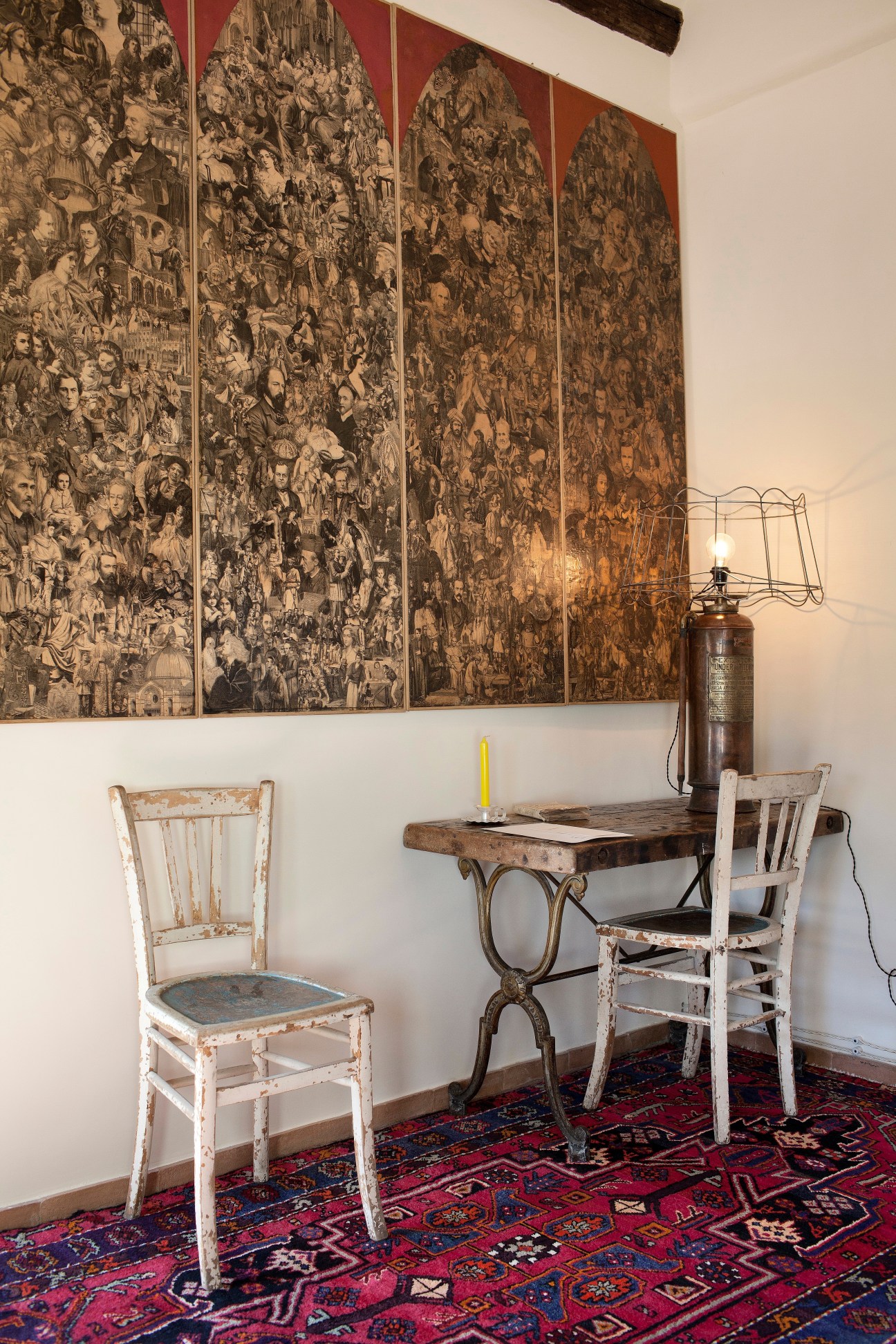 Historic hotel room with ornate tapestry wall art, whitewashed wooden chairs, and antique desk lamp.