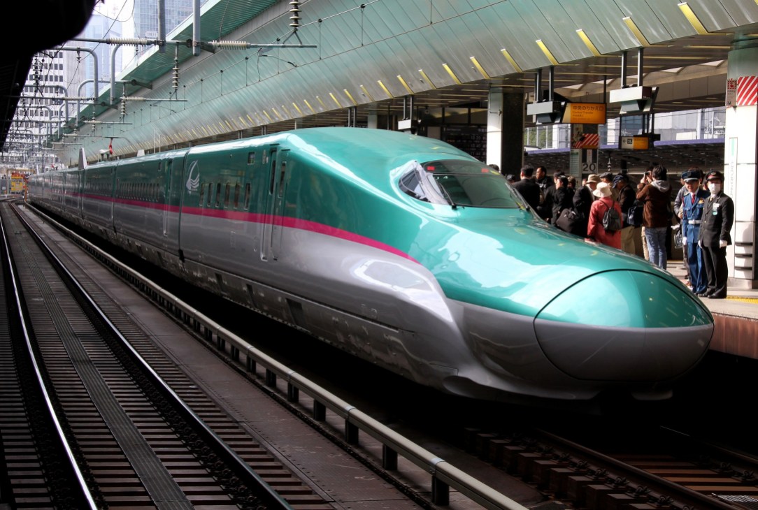 Turquoise and grey high-speed shinkansen train at platform with passengers boarding.