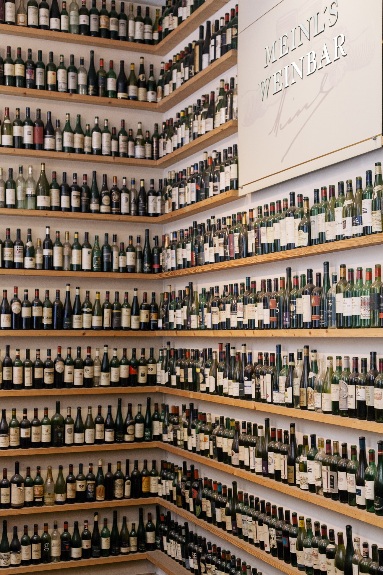 Meinl wine bar's extensive wine collection displayed on wooden shelves with illuminated signage