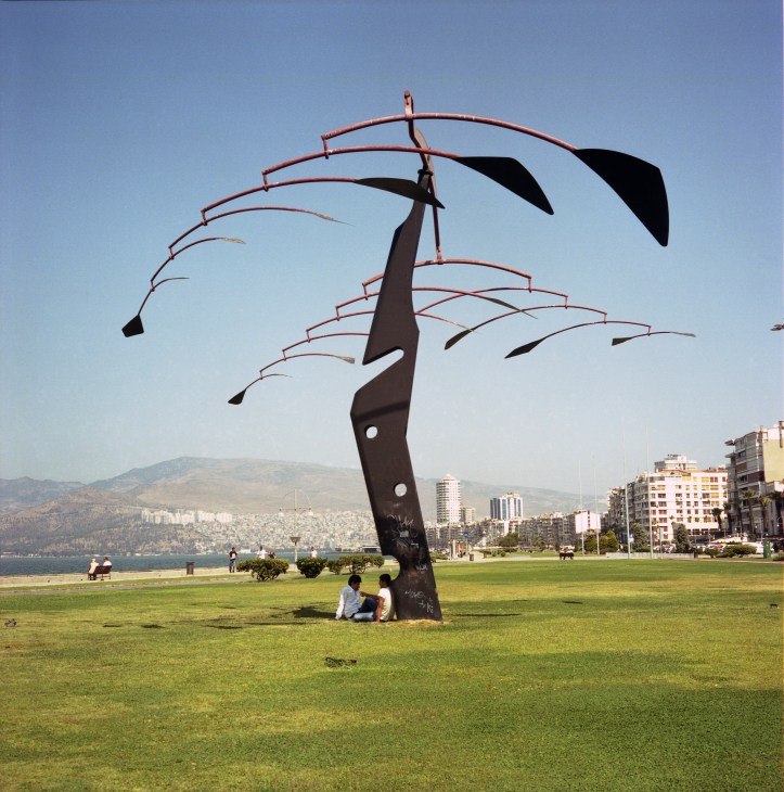 Modern sculptural art installation on Izmir waterfront with curved metal elements against clear sky and sea backdrop.