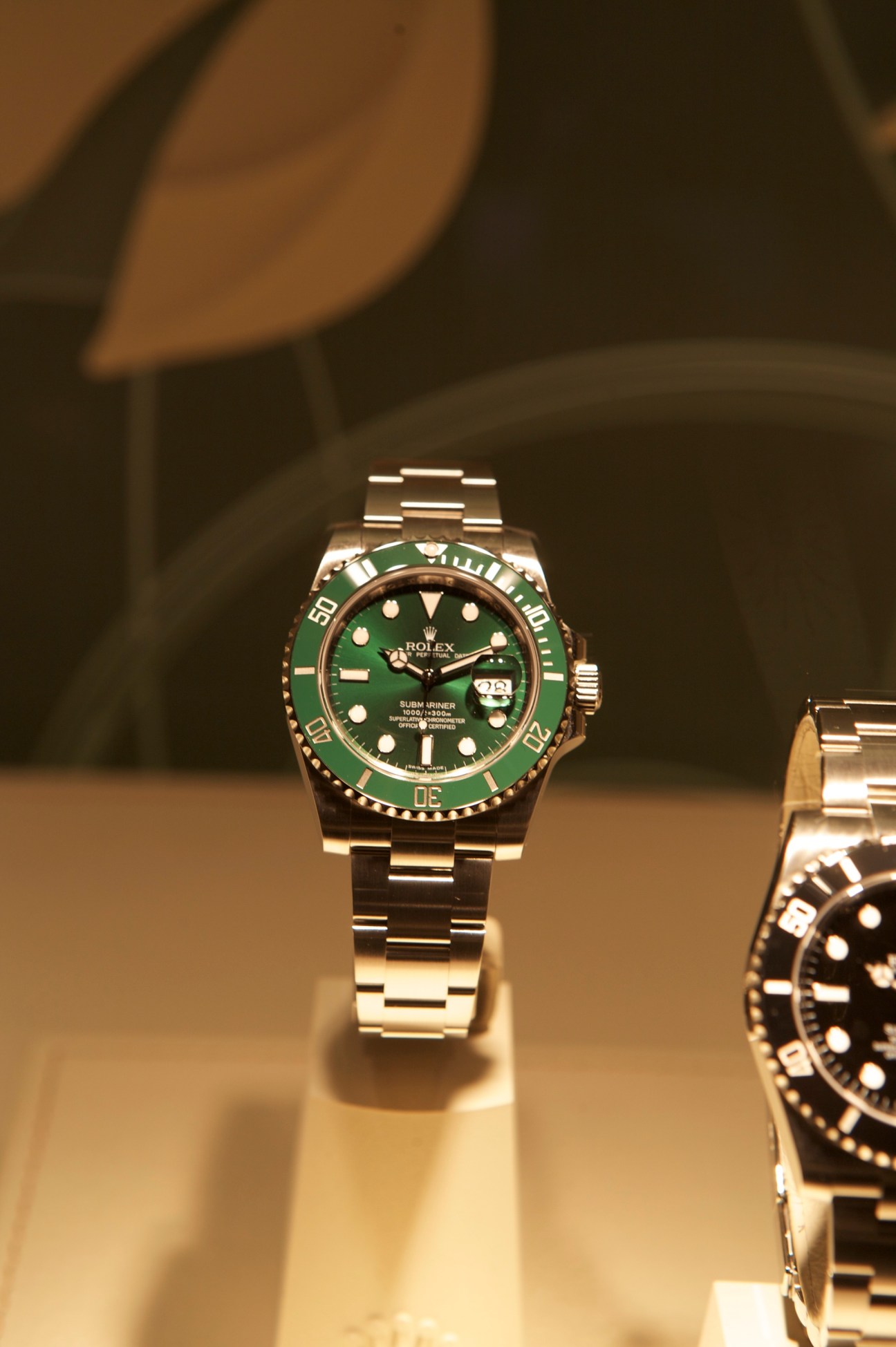 Rolex Submariner Date 40mm watch with green gold case and green bezel displayed on stand.