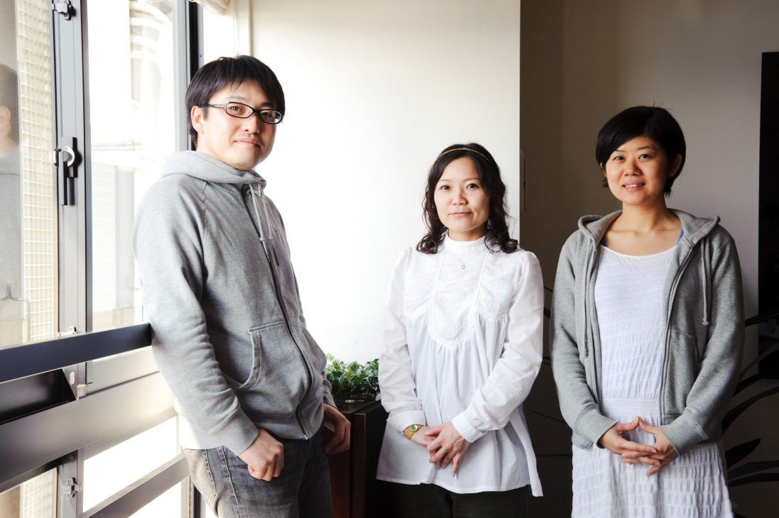 Three graphic designers and printers from Oiseau pose together by a window in an office space.
