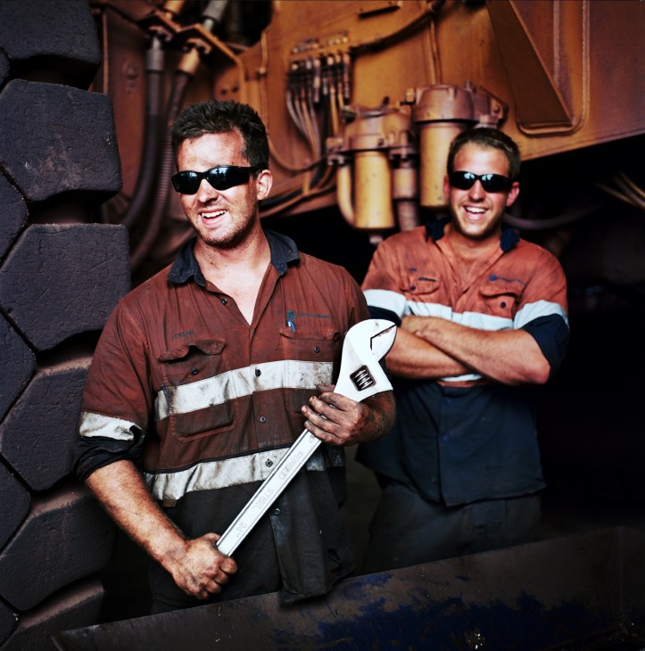 Two mechanics in work uniforms stand smiling inside mining equipment at Woodie Woodie Camp.
