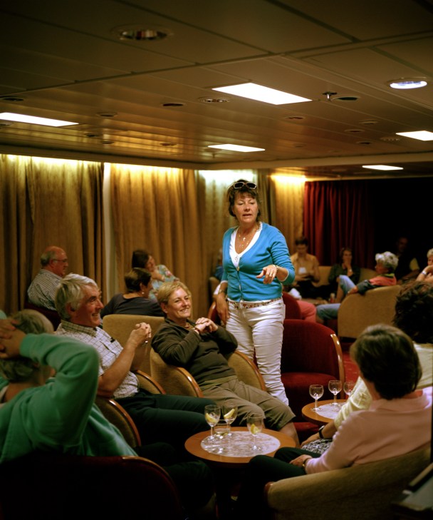 Passengers socializing in the main lounge of RMS St Helena with drinks after a trivia game.