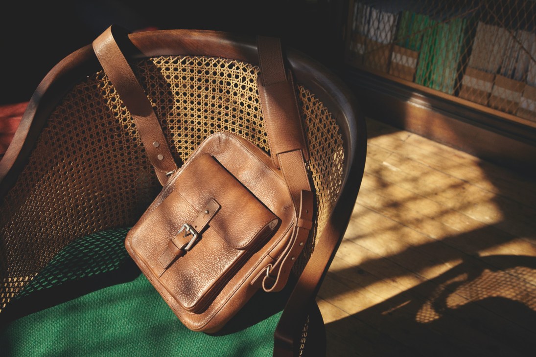 Brown leather satchel by Dunhill displayed on a woven chair with green fabric.