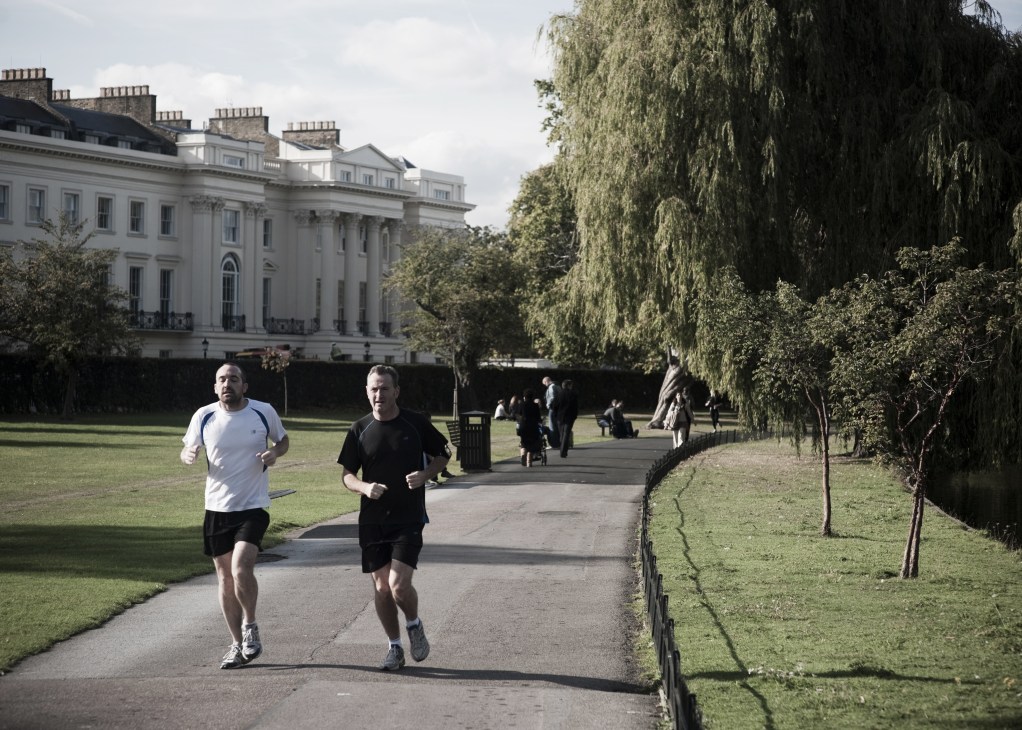 Two runners jogging in Regent's Park with Georgian buildings and weeping willow trees in the background.