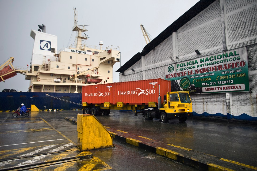 Cargo ship, containers and yellow truck at Buenaventura port with anti-narcotics police sign visible.