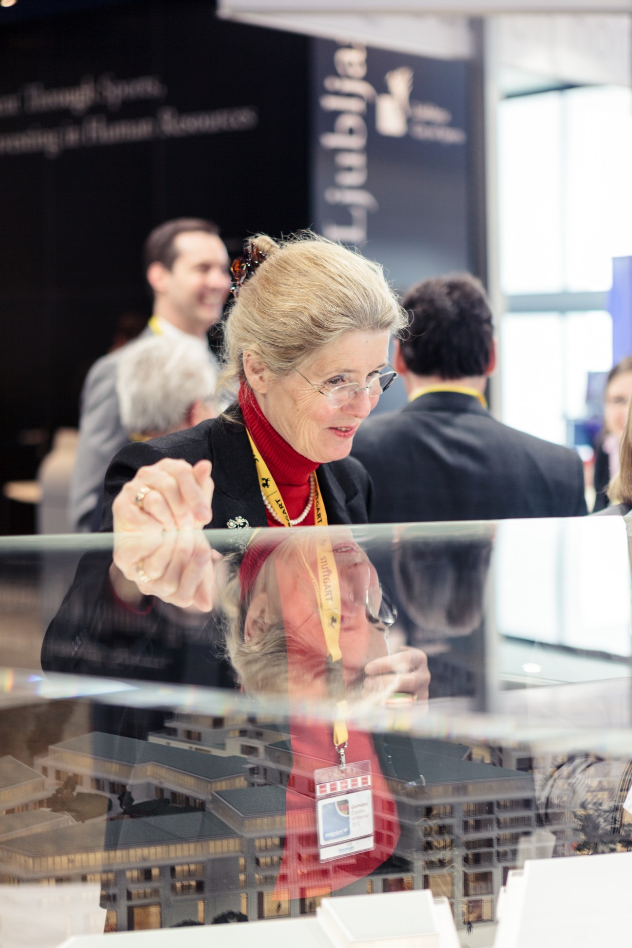 Woman in black blazer and red scarf examines architectural model at MIPIM conference.