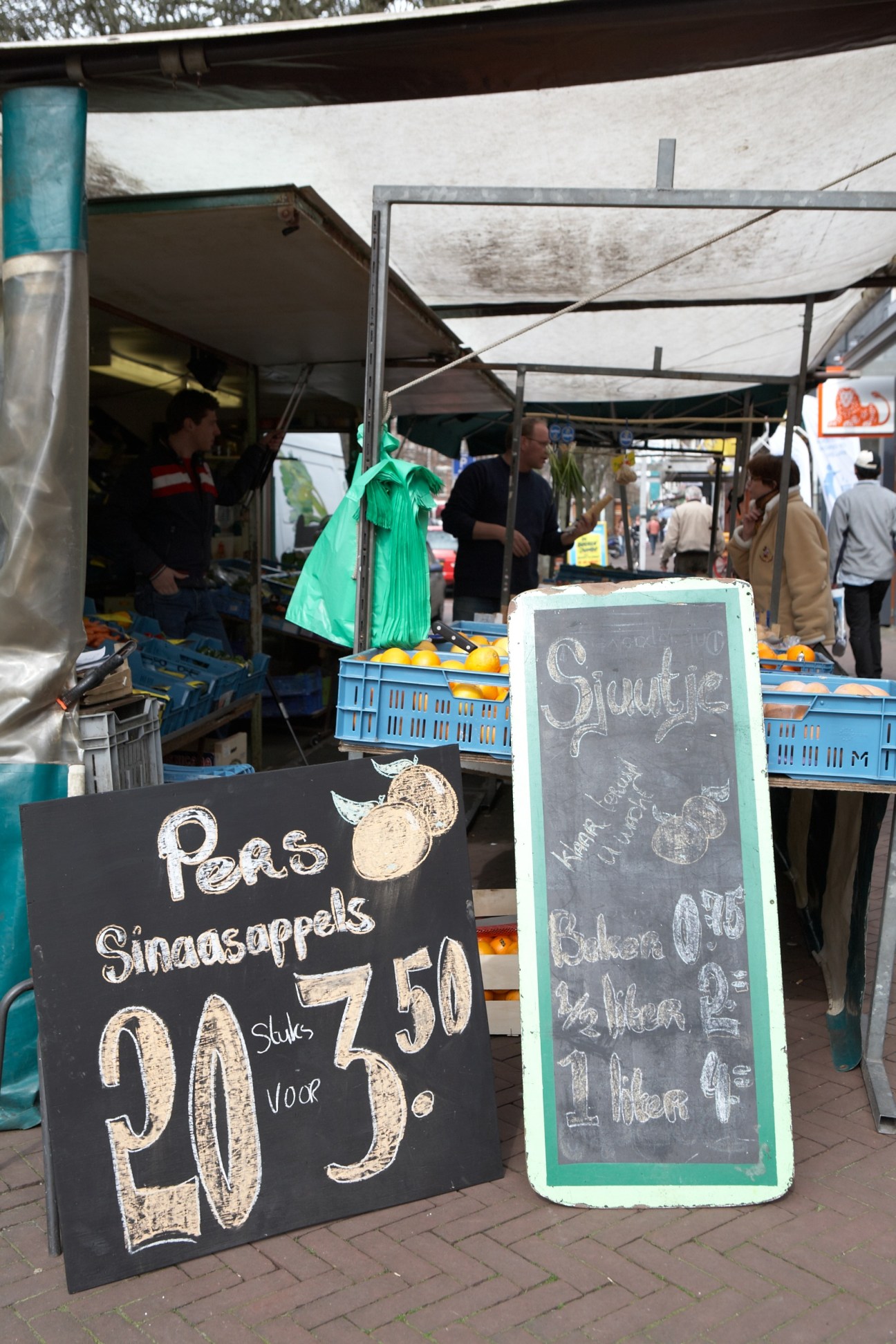 Market stall displaying handwritten price signs for pears and other produce at Brand fruit and vegetable market.