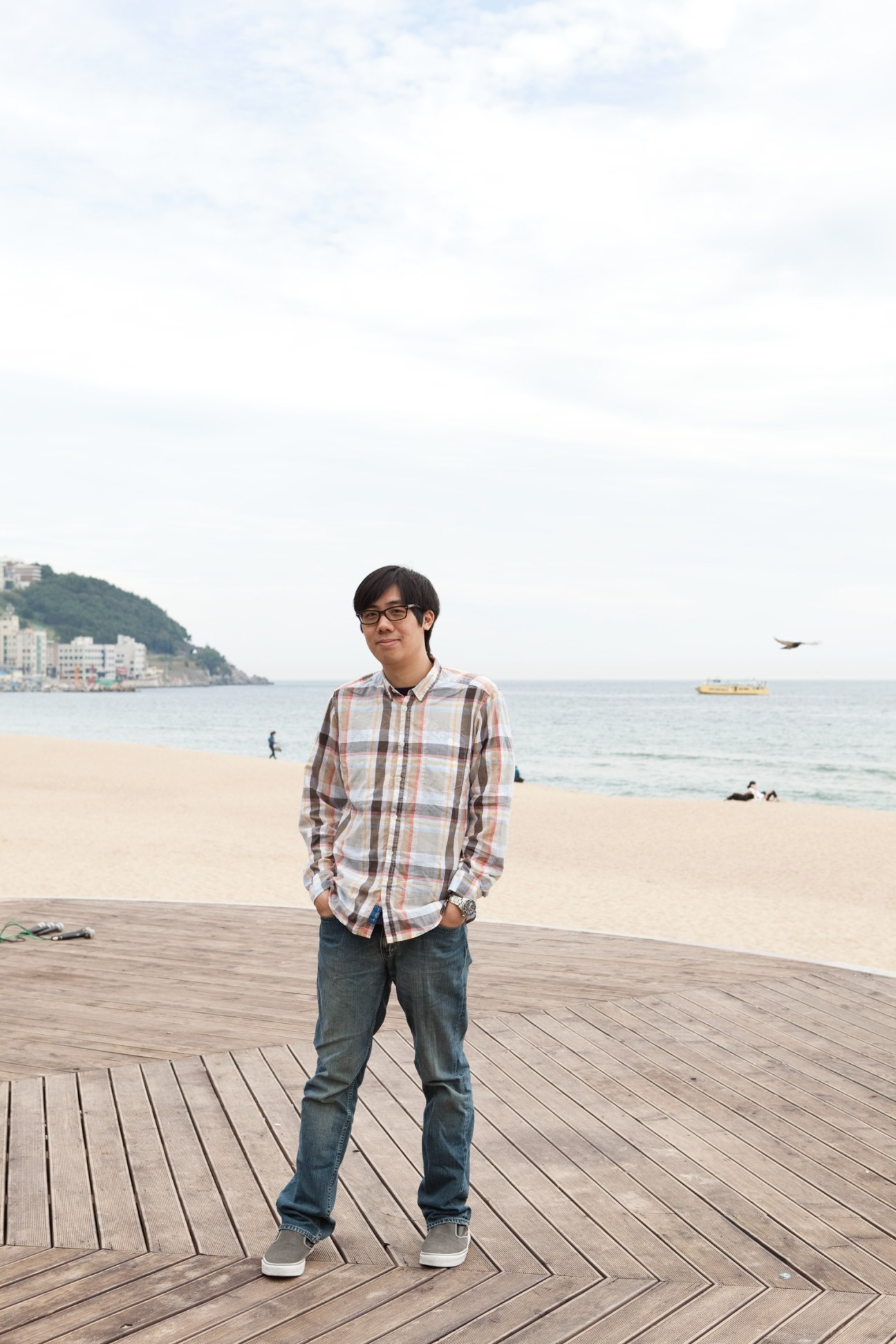 Taiwanese director Arvin Chen standing on a wooden deck at Haeundae beach in Busan with the ocean and coastline behind him.