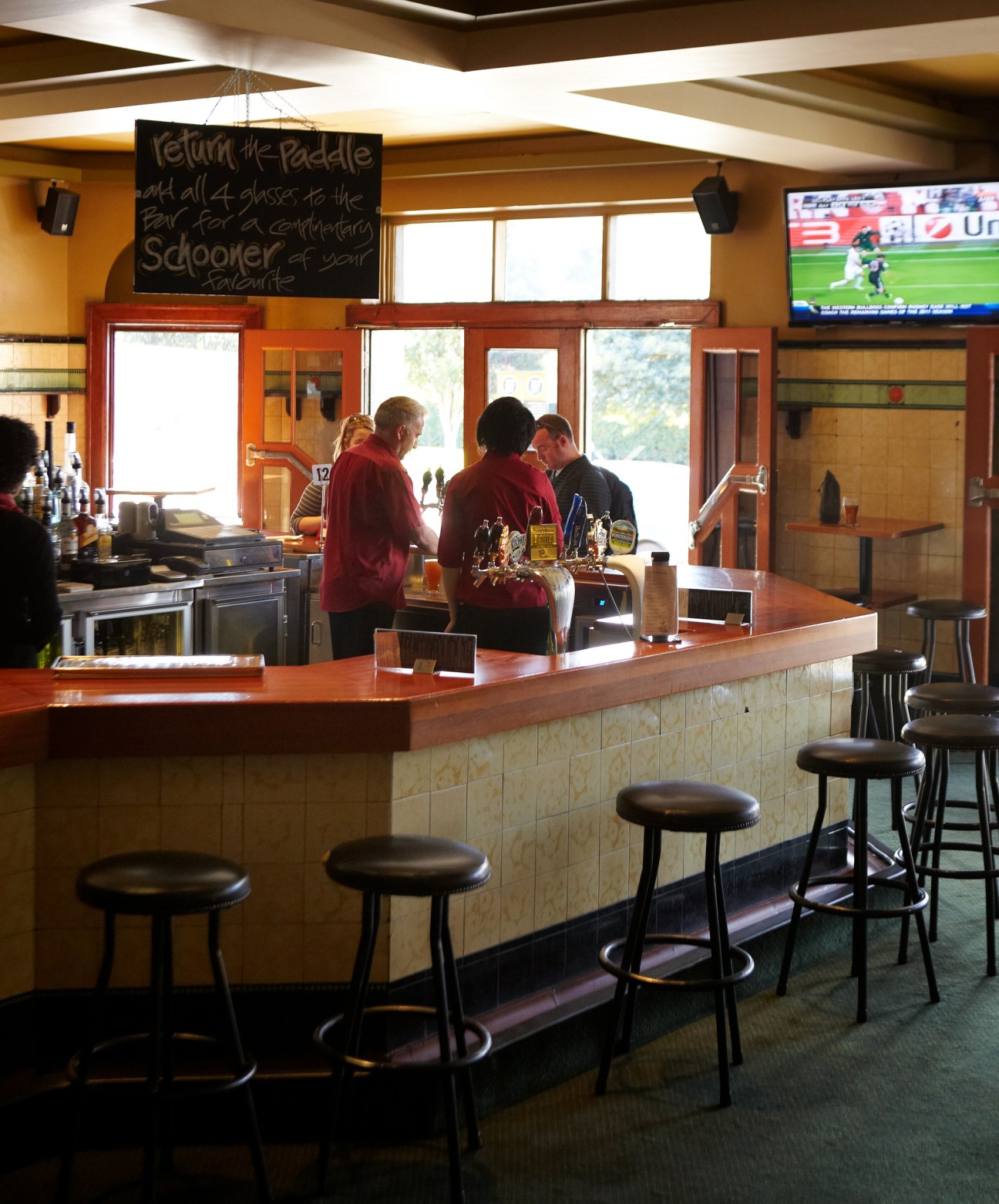 Interior of The Hive Bar with wooden counter, bar stools, and patrons in red shirts near the bar.