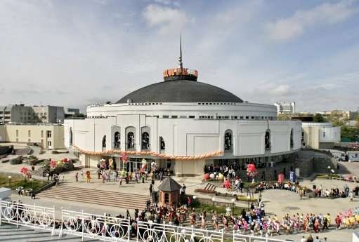 A white domed building with a golden spire surrounded by crowds of visitors in an outdoor plaza.