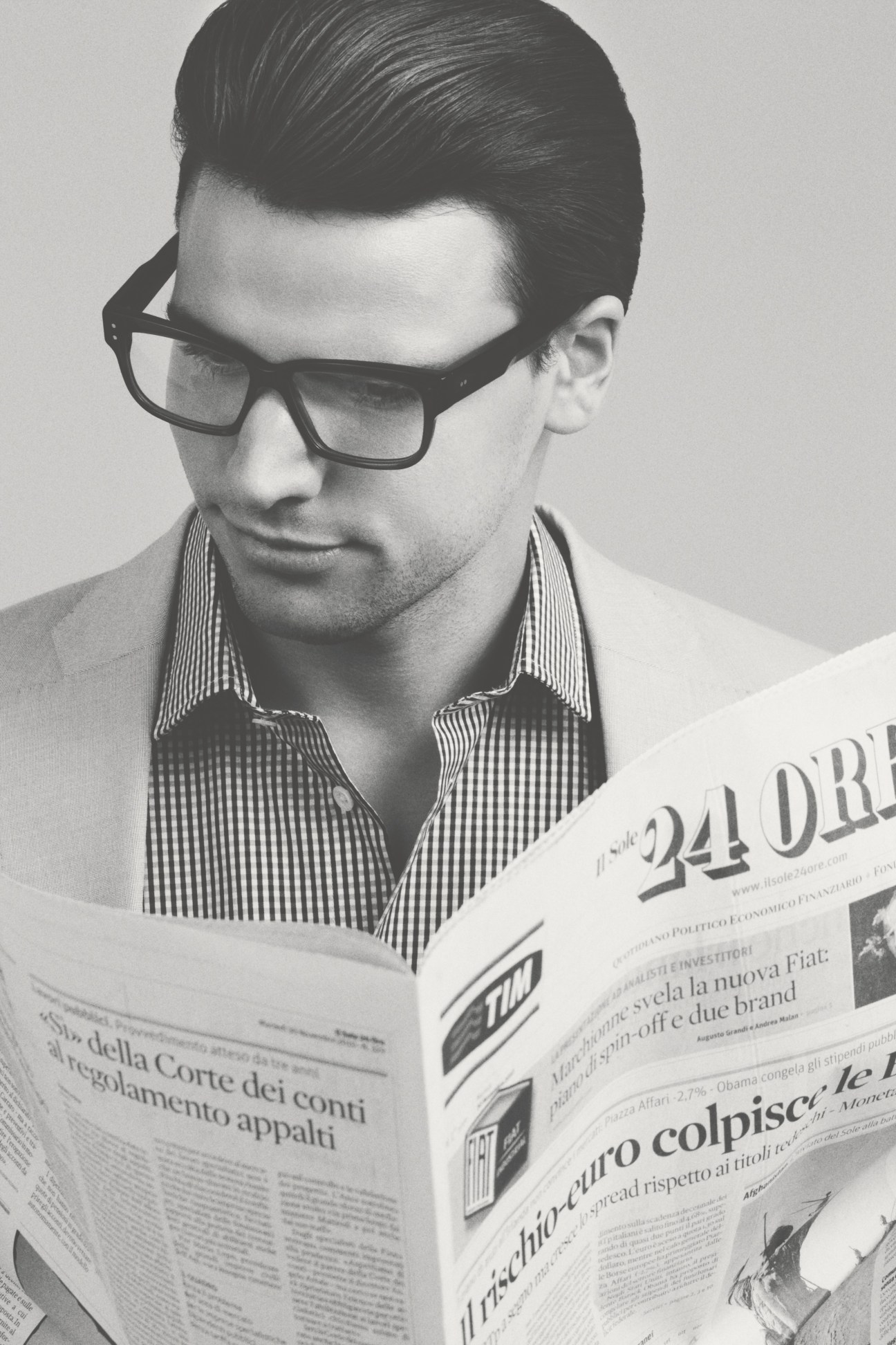 Man wearing Claire Goldsmith Watson glasses reading a newspaper in black and white.