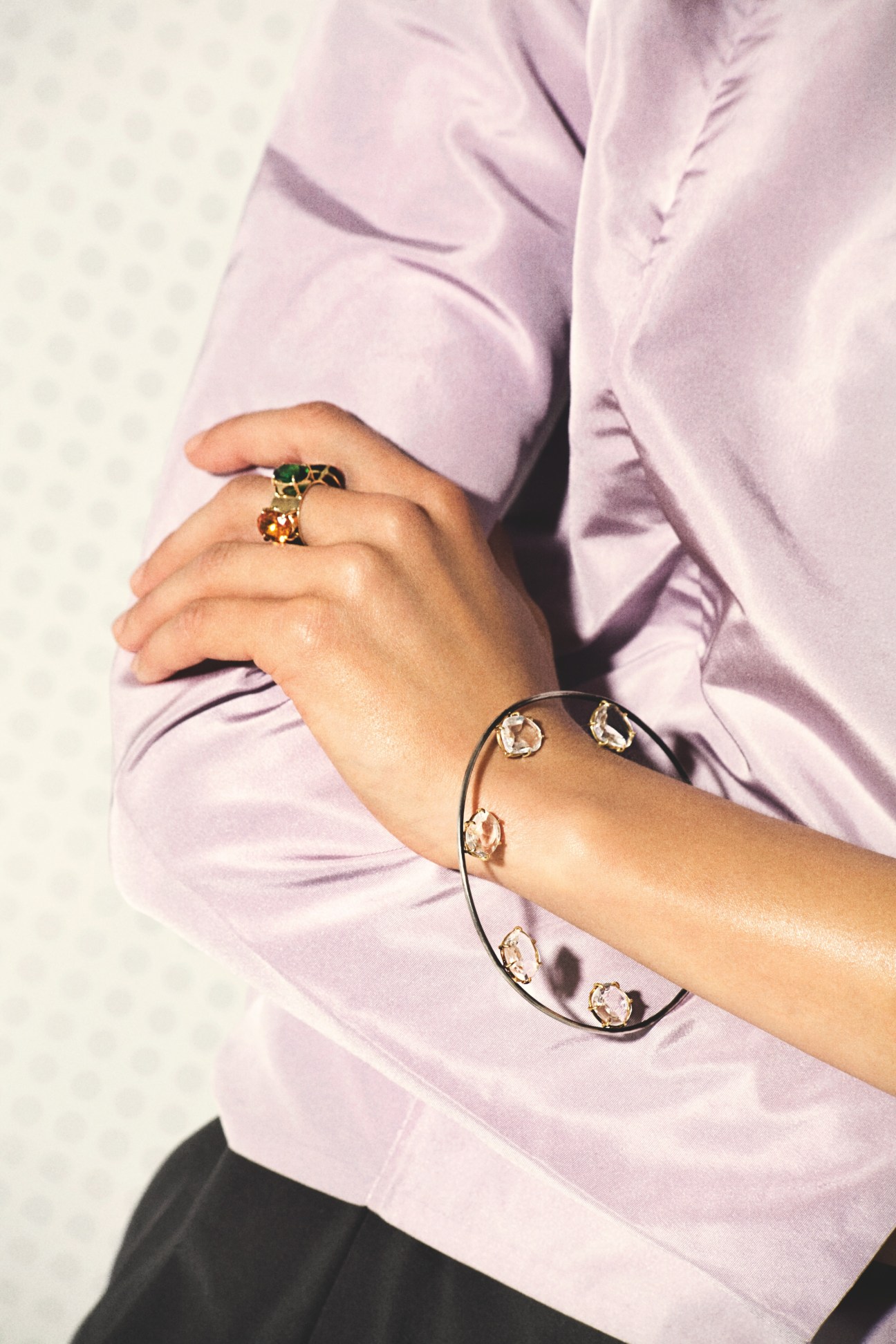 Person wearing a lavender shirt displaying a gold ring with tourmaline and a bracelet with rose-cut crystals by Dalila Barkache.