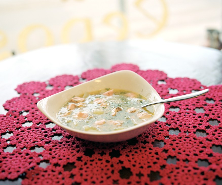 Salmon soup with vegetables in a white bowl on a red patterned placemat.