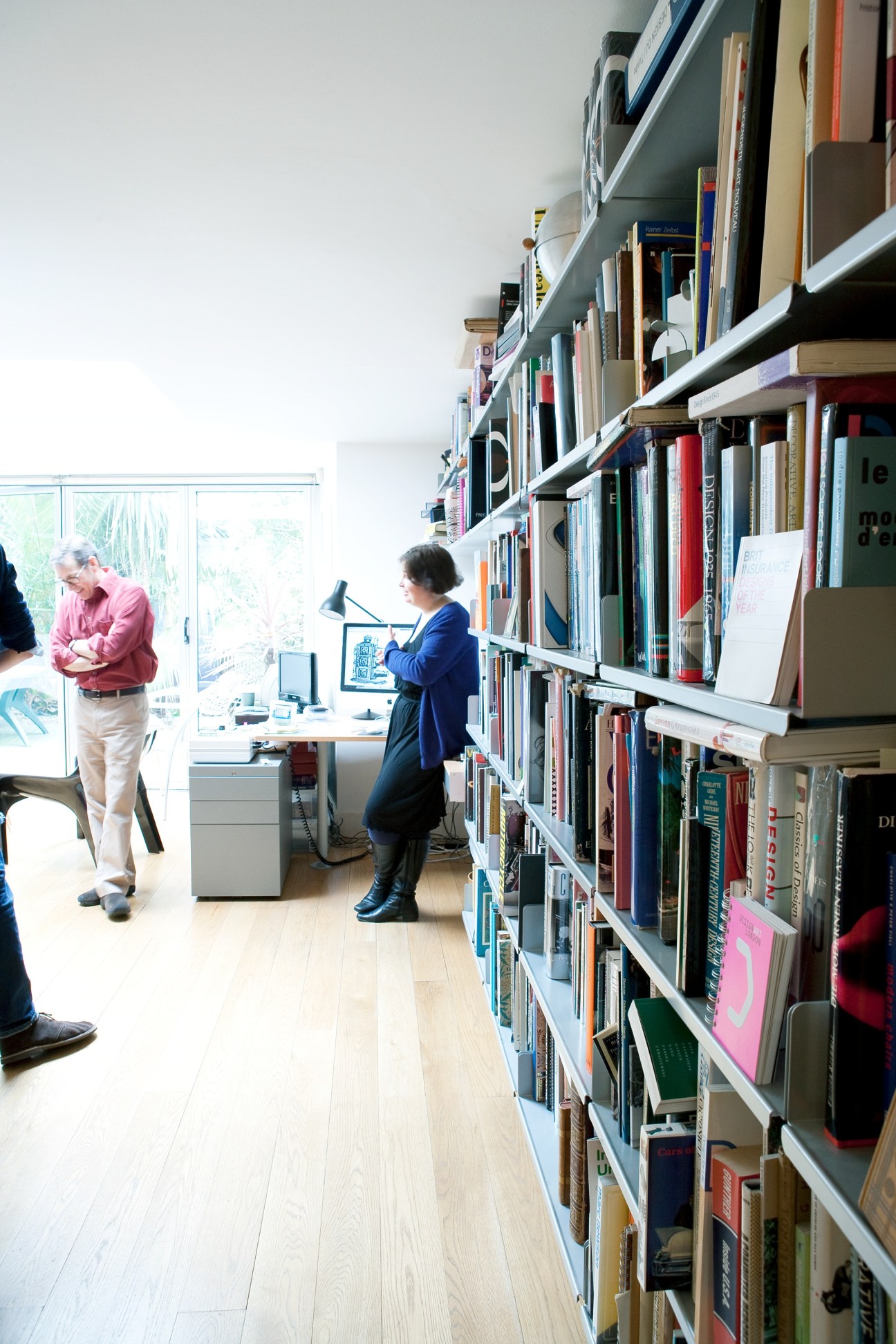 Charlotte Fiell stands in the Fiell office next to white shelving filled with design books.