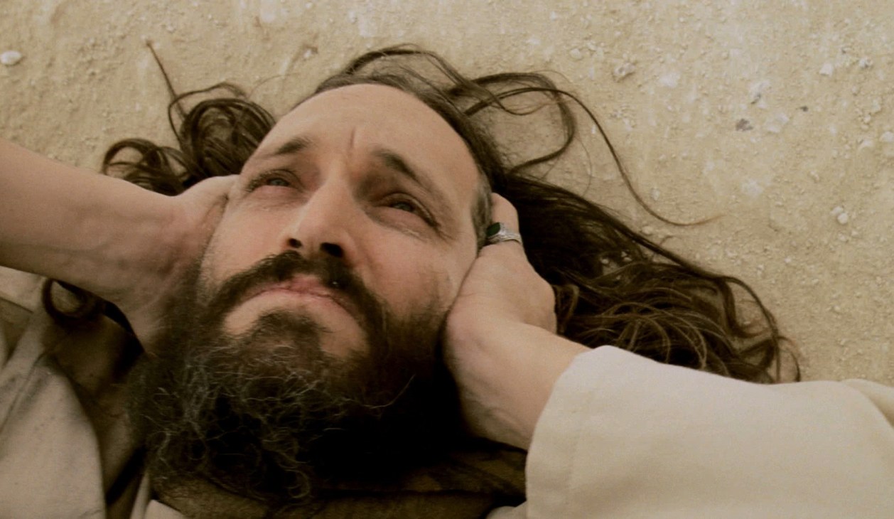 A bearded man with long hair lying on the ground in a scene from Essential Killing.