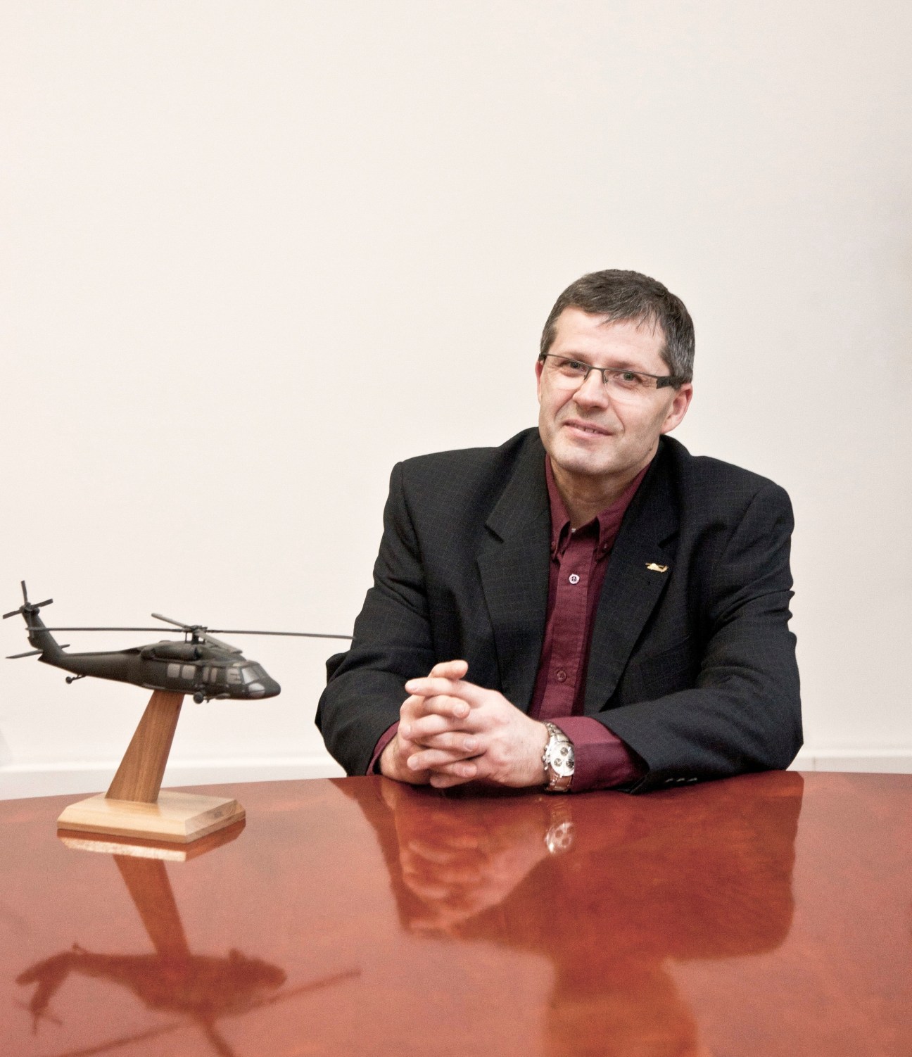 PZL Mielec's CEO Janusz Zakrecki sits at a desk with a helicopter model, wearing glasses and dark blazer.
