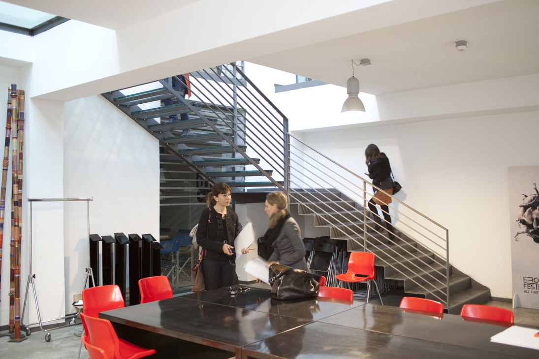 Modern office interior with red chairs, black table, and industrial staircase with people working.