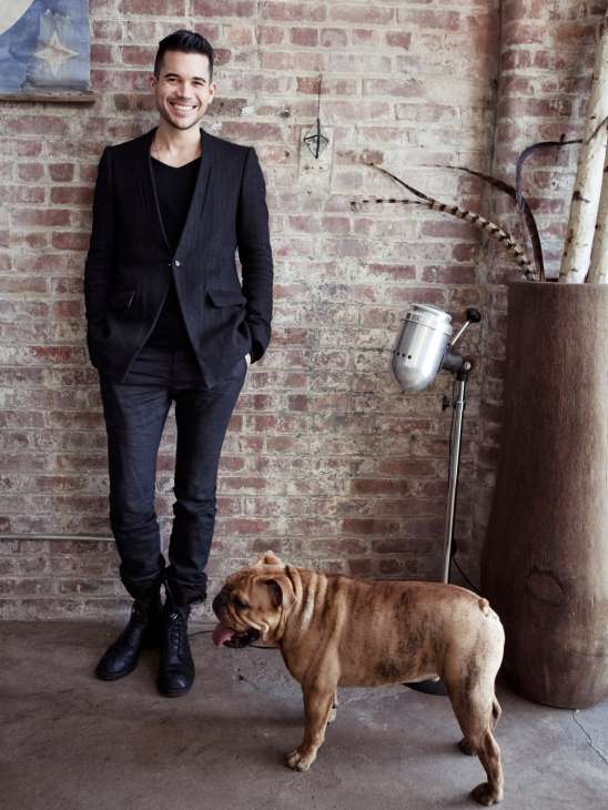 Matthew Dear stands against a brick wall with his dog Artie in a studio setting.