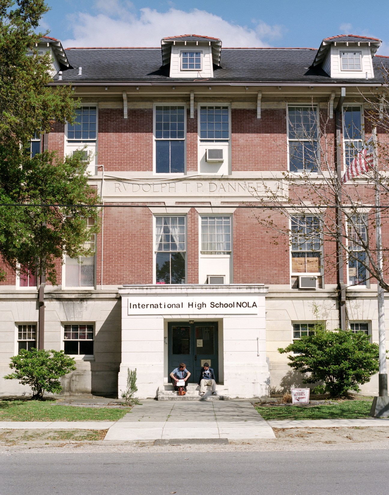 International High School NOLA building entrance with two students sitting on steps