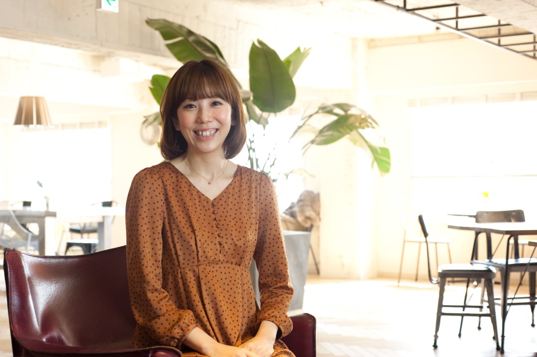 Satoko Inoue, ReBITA project manager, smiling in The Share's communal lounge area with plants and modern furniture.