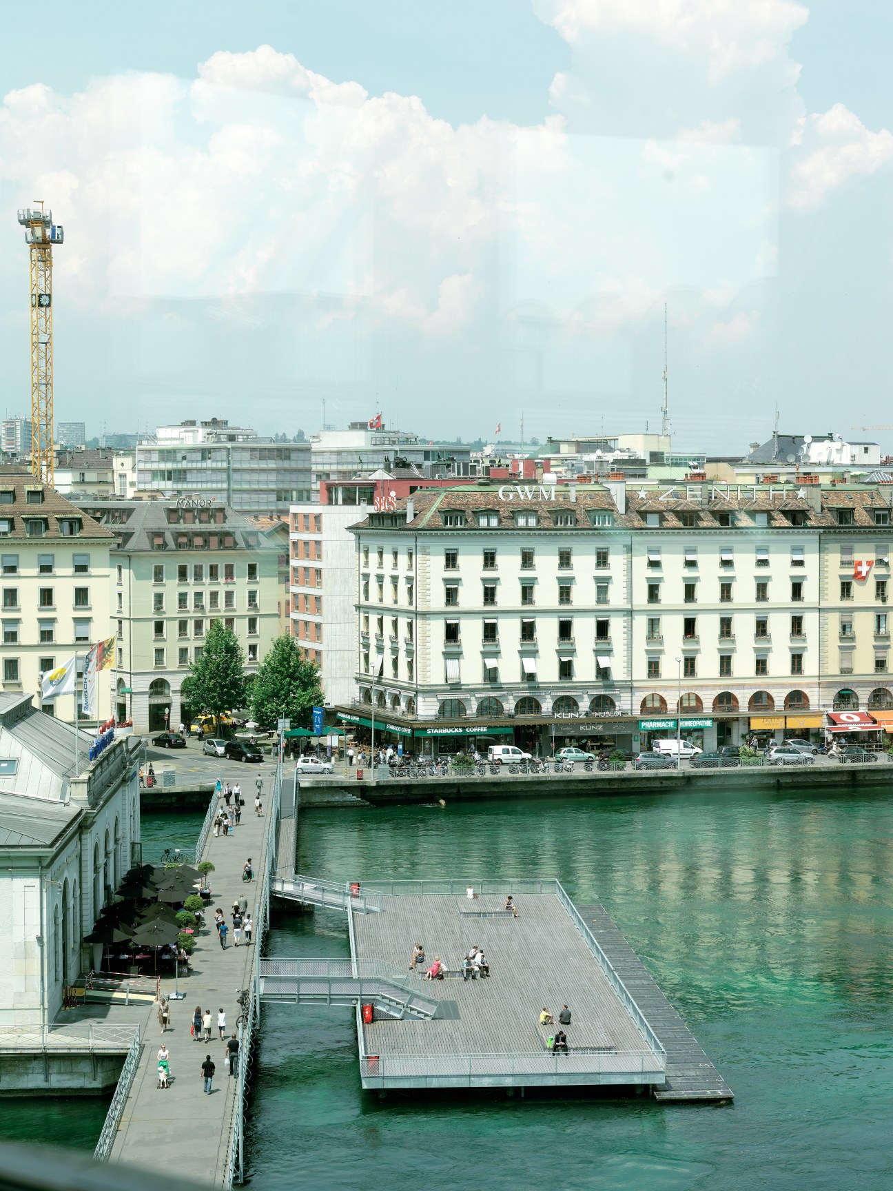 Geneva's waterfront with turquoise lake, classical buildings, and summer crowds on the promenade.