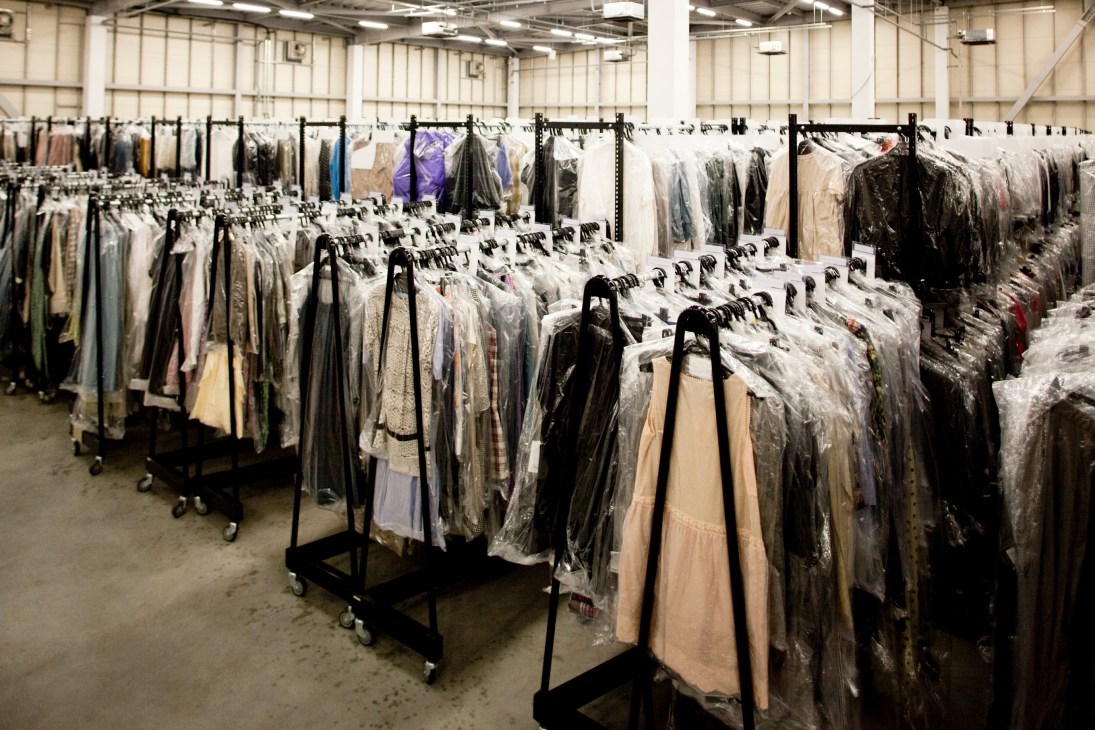 Rows of hanging racks filled with plastic-wrapped clothing items in a large warehouse space.