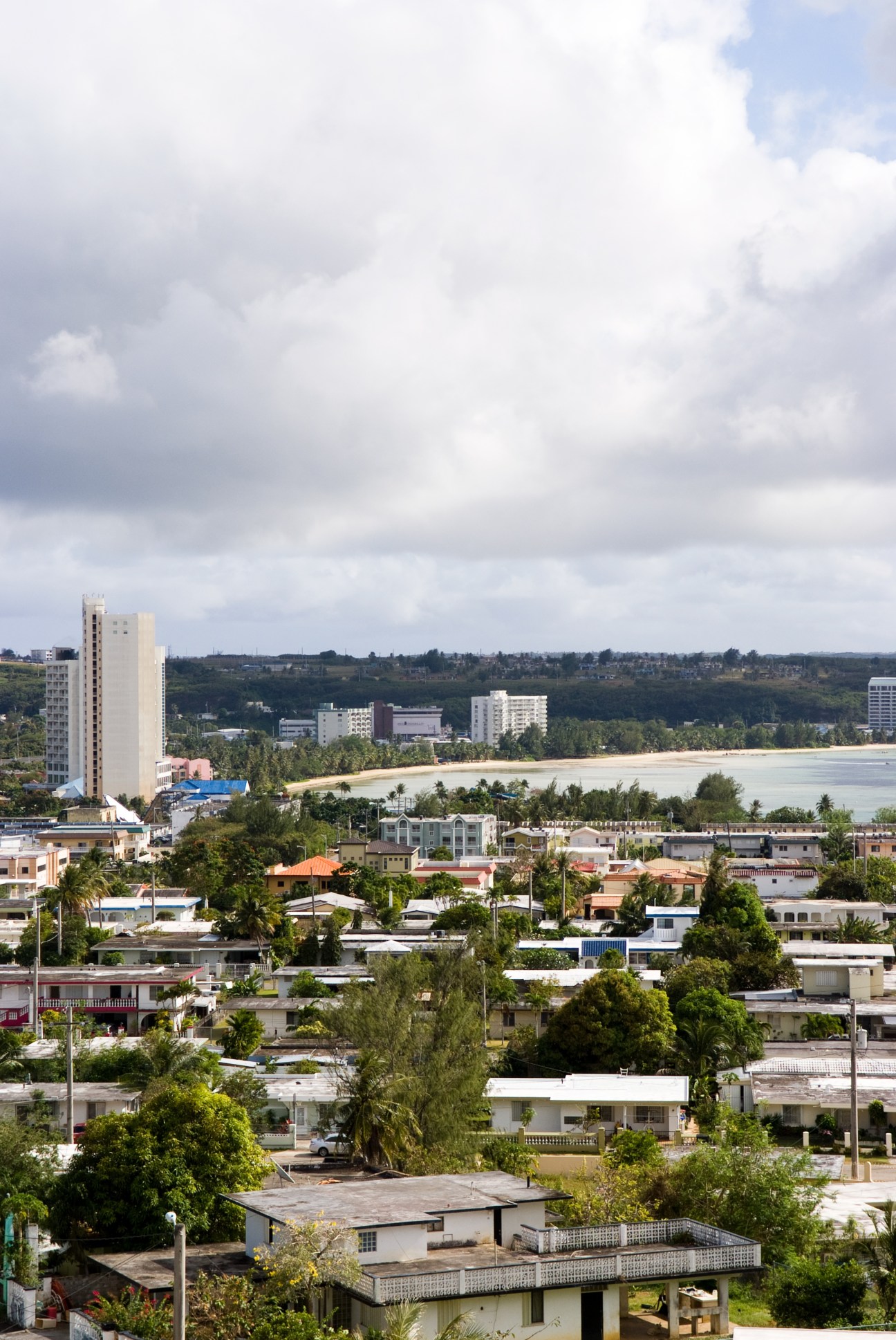 Guam's western coast showing high-rise hotels, residential buildings, and beach with palm trees.