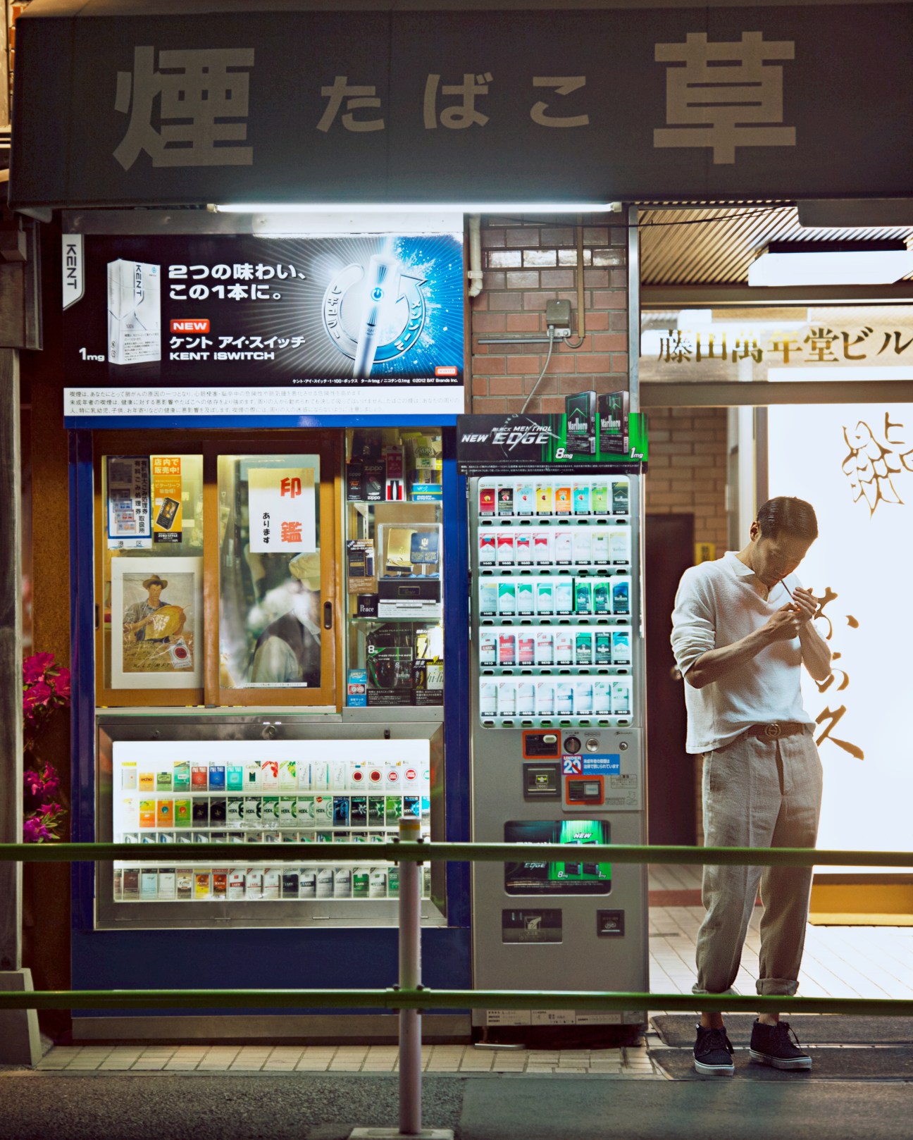 Man in light clothing using a vending machine on a Tokyo street at night.