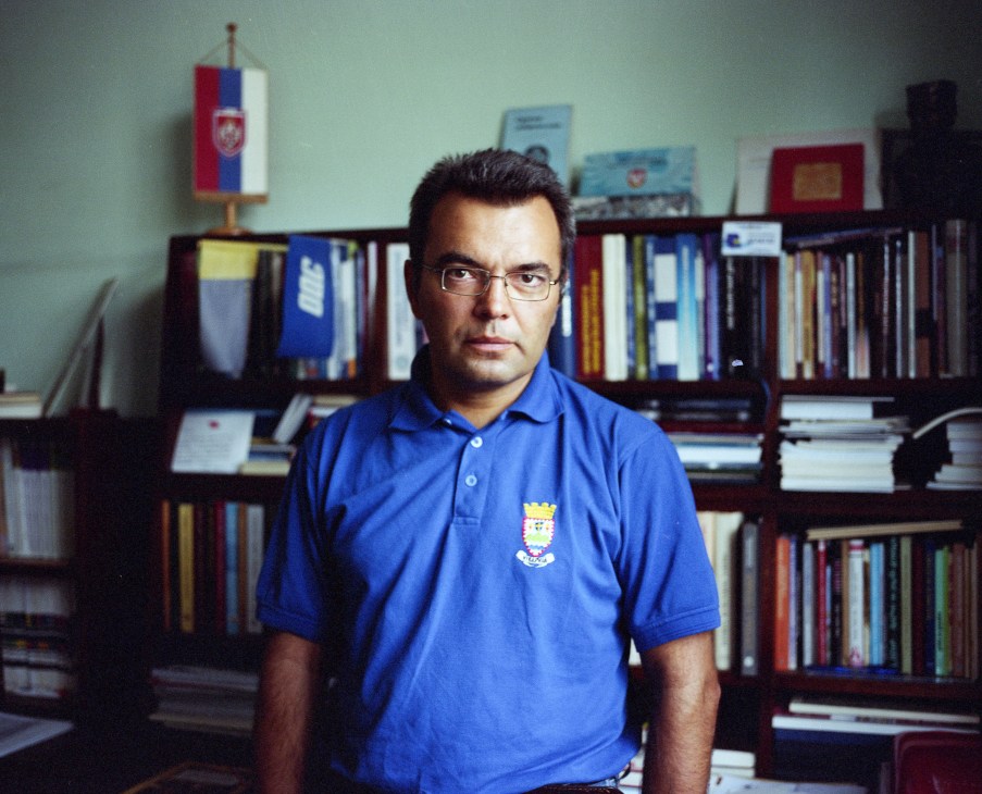 Historian Bojan Dimitrejevic in his office with bookshelves and Serbian flag.