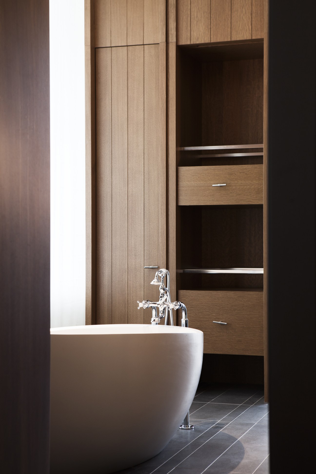 Modern white egg-shaped soaking tub with chrome fixtures in the Splash Suite bathroom, with wooden storage cabinetry behind.