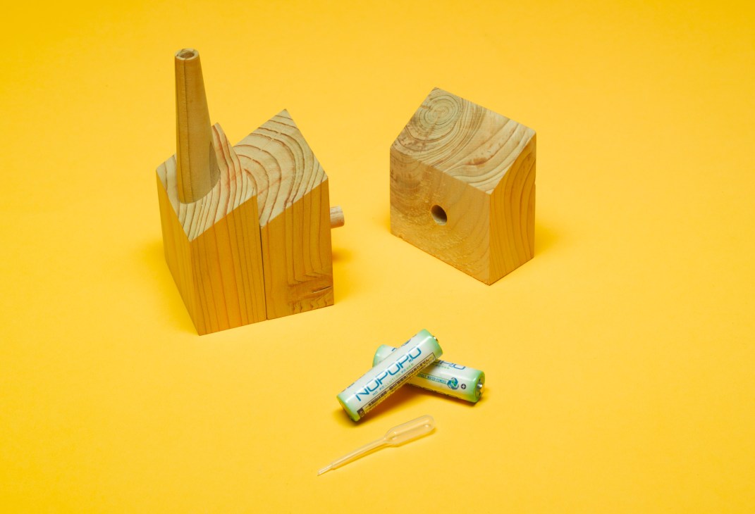 Wooden cedar blocks with house-shaped design, batteries, and a small tool on yellow background.