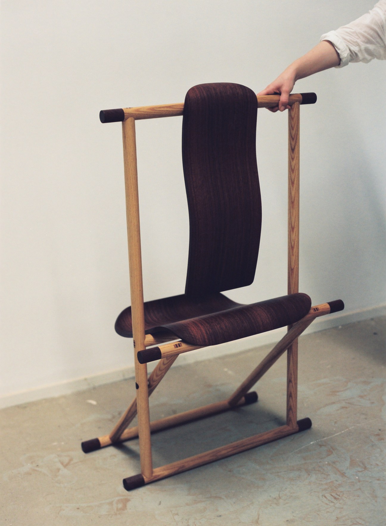Wooden chair by Brianna Russell with dark upholstered seat and backrest on light ash frame.