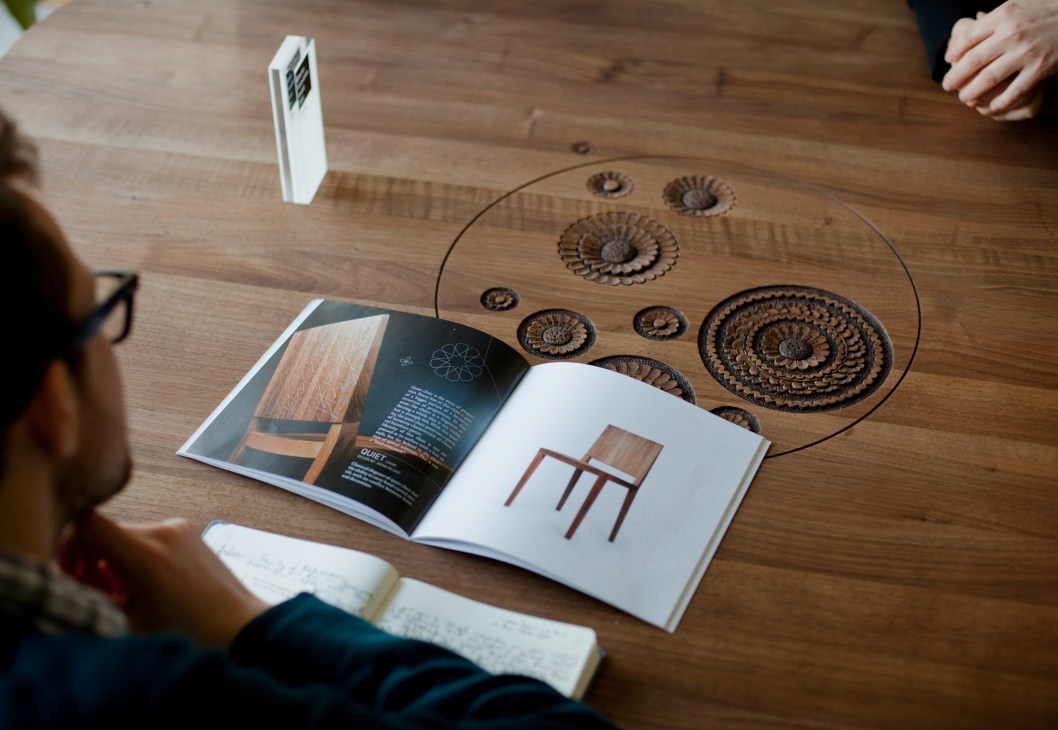 Rukotvorine catalogue displayed on a wooden Wave table with carved circular designs, alongside a white business card holder.